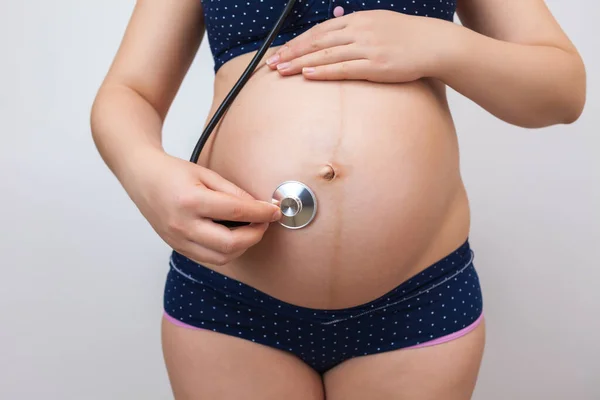 Pregnant woman with a stethoscope listens to her baby's heartbeat