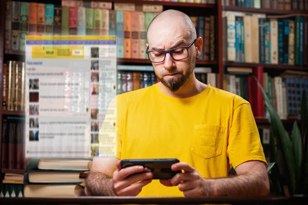 A bearded bald man with glasses uses a smartphone with a frown. Digital transparent window above the phone. The concept of a social network, distance learning, and self-isolation.