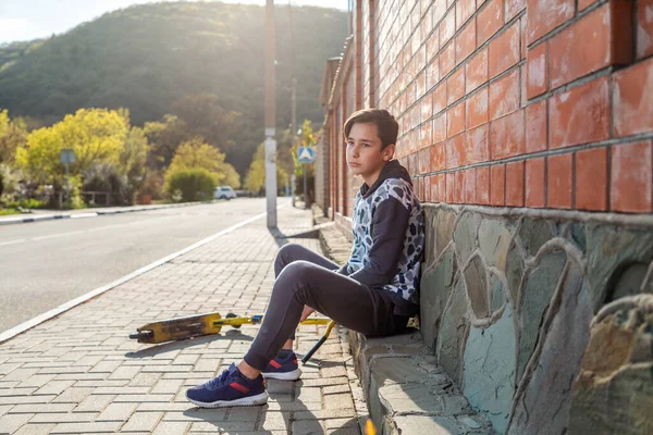 Ein Halbwüchsiger Junge Sitzt Auf Dem Gehweg Neben Einem Motorroller — Stockfoto