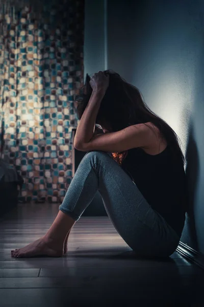 家庭内暴力と女性の不平等の概念 若い女性が暗い部屋の床に座って頭を握りしめている 背景にはカーテン付きの窓があります — ストック写真