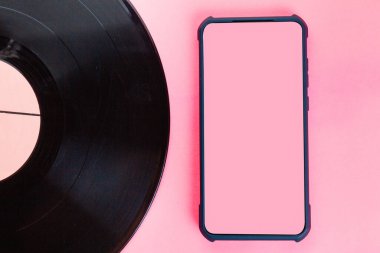 Pembe arka planda vinil disk ve akıllı telefon. Düz yatıyordu. Uzayı kopyala ve taklit et. Müzik teknolojisinin evrimi kavramı.