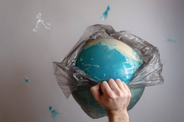 Bir adam, Dünya gezegeninin sarılı olduğu bir çöp torbasını kırar. Çevredeki çevre kirliliği ve ekoloji kavramı. Boşluğu kopyala.