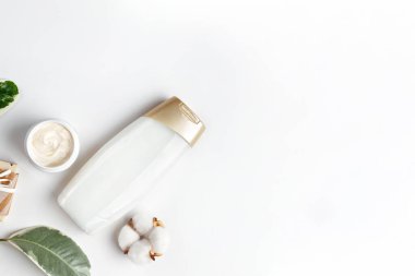 Kozmetik ve kişisel bakım. Beyaz arka planda yeşil yapraklar, duş jeli, krem ve pamuk çiçeğinden oluşan bir kompozisyon sergilenmektedir. Düz yatıyordu. Uzayı kopyala Yatay.