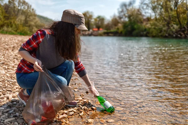 Woman volunteer helps clean the shore of river of garbage. Earth day and environmental improvement concept. Eco. Tint.