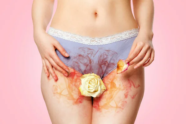 一个女人穿着内裤 两腿中间夹着一朵白玫瑰花 散发着一股难闻的香味 手里拿着一朵枯萎的花瓣 靠近点粉色背景 更年期的概念和妇女的健康问题 — 图库照片