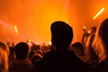 Konserde bir kalabalık eğleniyor ve konserde müzik eşliğinde dans ediyor. Arka planda turuncu ışık var. Dikiz aynası. Eğlence ve rahatlama kavramı.