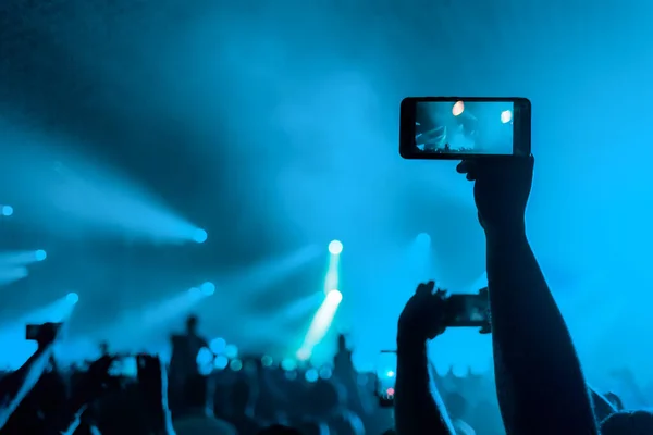 人はスマートフォンでコンサートを撮影します 手を閉じて 後ろの景色 青の背景 エンターテイメントと現代技術の概念 — ストック写真