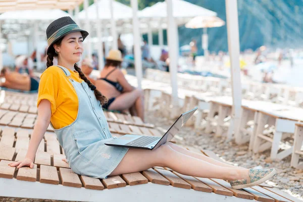 F.reelance. A young woman sits relaxed on a sunbed with a laptop on her lap. Summer holiday