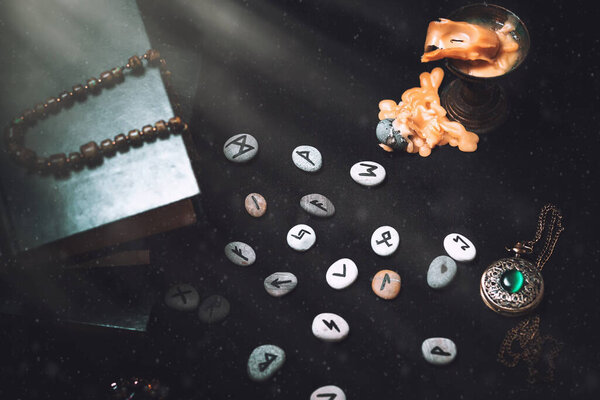 Astrology and esotericism. On a black background lie fortune-telling runes, a book, an amulet, and a candle. Light. Top view.