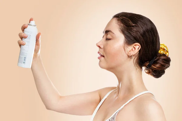 若い白人女性 ぬれた肌で 化粧品のボトルを保持 コピースペース サイドビュー ベージュの背景 スキンケア 日焼けの概念 — ストック写真