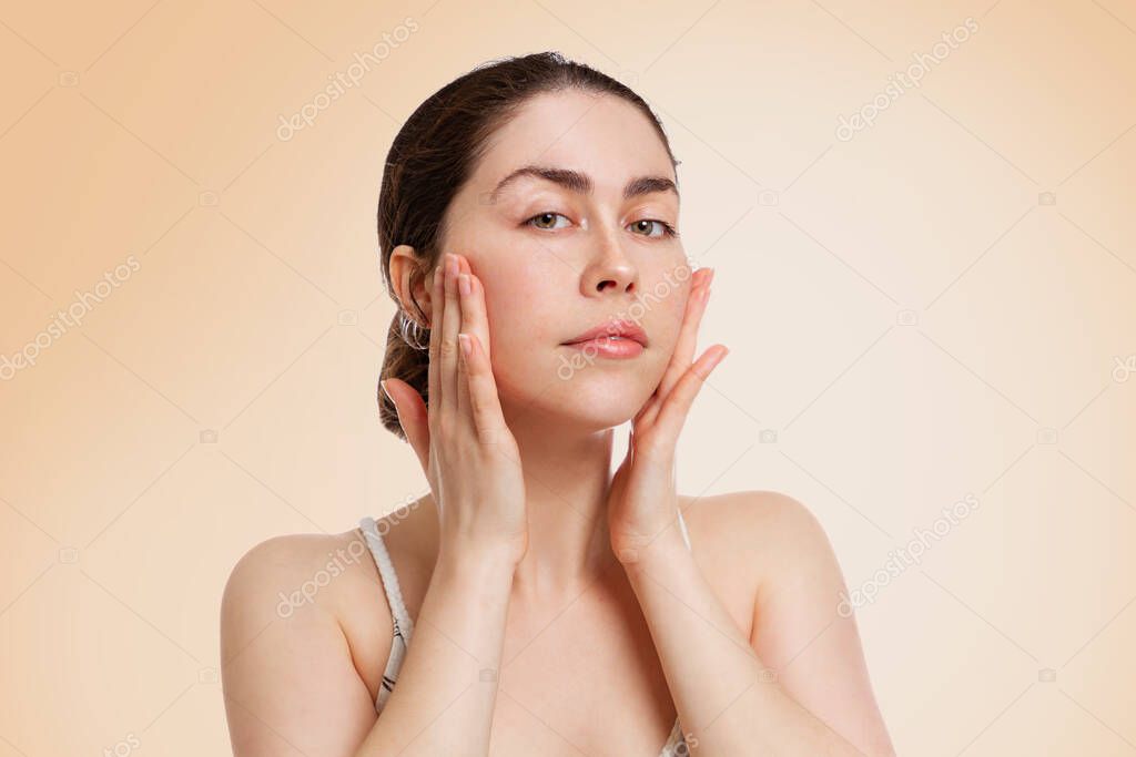 Portrait of a young woman with beautiful skin, pulling the skin on her cheeks with her hands.Beige background. Copy space. Concept of beauty, rejuvenation and cosmetology.
