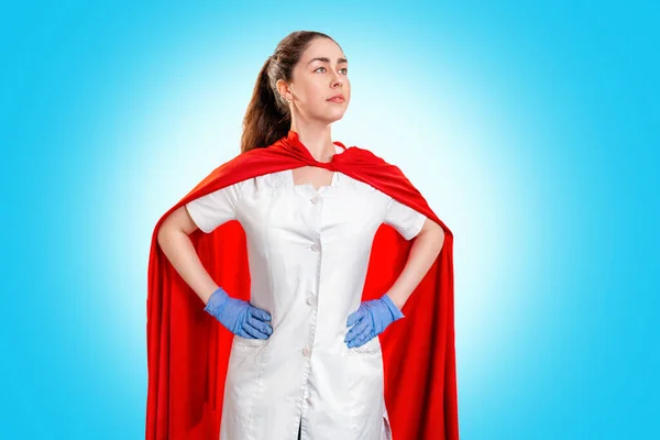 A doctor wearing a medical gloves, and a superhero red cape stands guard over health. Blue background. Copy space. The concept of the Power of a super hero for medicine.