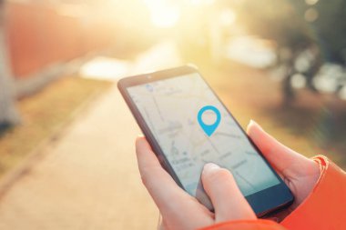İnternet haritası ve navigasyon kavramı. Kadınların elinde harita uygulaması olan bir akıllı telefon ve konumun işaretli bir simgesi var. Işık.