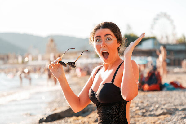 Портрет женщины держит солнечные очки и крики от солнечных ожогов. Покраснение на коже лица и тела. На заднем плане пляж и море. Концепция защиты и ухода за кожей
.
