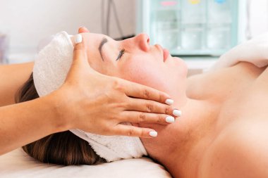 Bir kozmetik uzmanı bir kadın için yüz masajı prosedürü uygular. Müşterinin yüzünü yakından çek. Kozmetoloji ve tedavi kavramı.