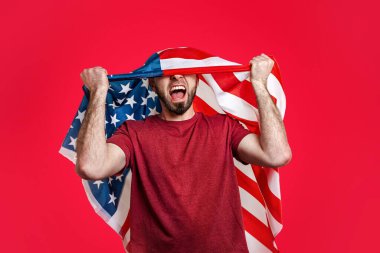 Kafasında Amerikan bayrağı olan beyaz bir adam ellerini kaldırıp bağırıyor. Kırmızı arka plan. Vatanseverlik, güç, özgürlük ve spor fanatikleri kavramı.