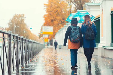 Sokakta iki kadın şemsiye altında yürür. Yağmurlu bir hava. Sonbahar.