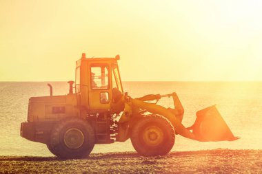 Plajda buldozer gezintisi. Arka planda deniz ve gökyüzünde. Renk.