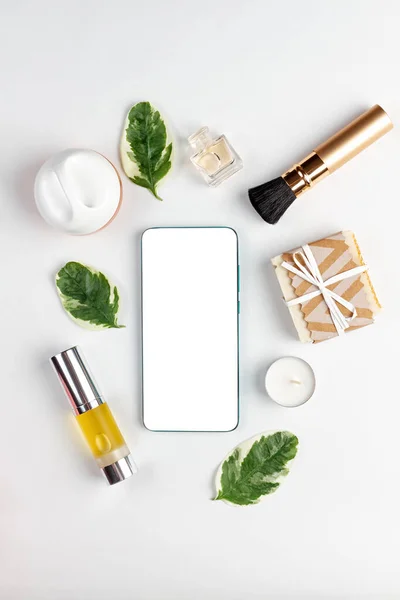 On a white background is cosmetics, leaves, candles and a smartphone. Flat lay. Vertical. Mock up. Concept of beauty, cosmetics and modern technologies.