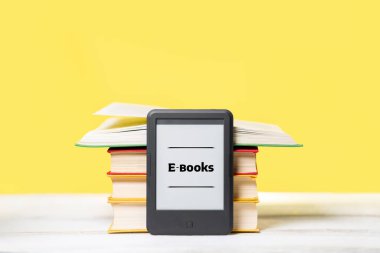- Bilgi. E-kitap okuyucu ve sarı arka planda bir yığın kitap. Uzayı kopyala Eğitim ve elektronik aletler kavramı.