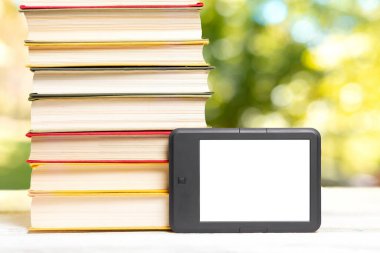 Okuma ve bilgi. E-kitap okuyucu ve bir yığın kitap. Park arka planda bulanık. Model yap. Eğitim ve elektronik aletler kavramı.