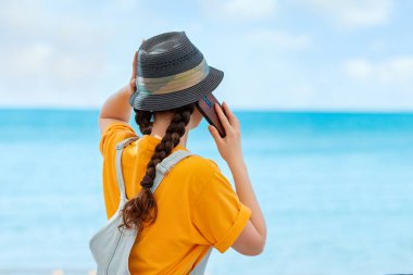 Cep telefonunda hasır şapkalı bir kadın arıyor. Dikiz aynası. Arka planda deniz ve gökyüzü. Uzayı kopyala Tatil ve iletişim kavramı.
