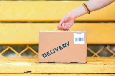 Kurye bankın üzerine barkodlu bir karton kutu koyar. El ve paket yakın planda. Ekspres teslimat kavramı.