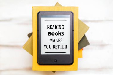 Okuma ve bilgi. E-kitap okuyucu ahşap bir arka plandaki kitap yığınının üstünde. Düz yatıyordu. Eğitim ve elektronik aletler kavramı.
