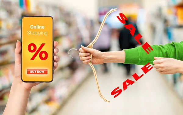 Females hands hold a hanger in the form of a hunting bow. Side view. Cellphone with advertising of sales. Concept of sale and hunting for discounts.