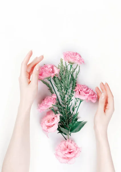 Delicate female hands frame the scattered pink buds of eustoma. White background. Flat lay. The skin is albino. Copy space. The concept of Floristics and tenderness.