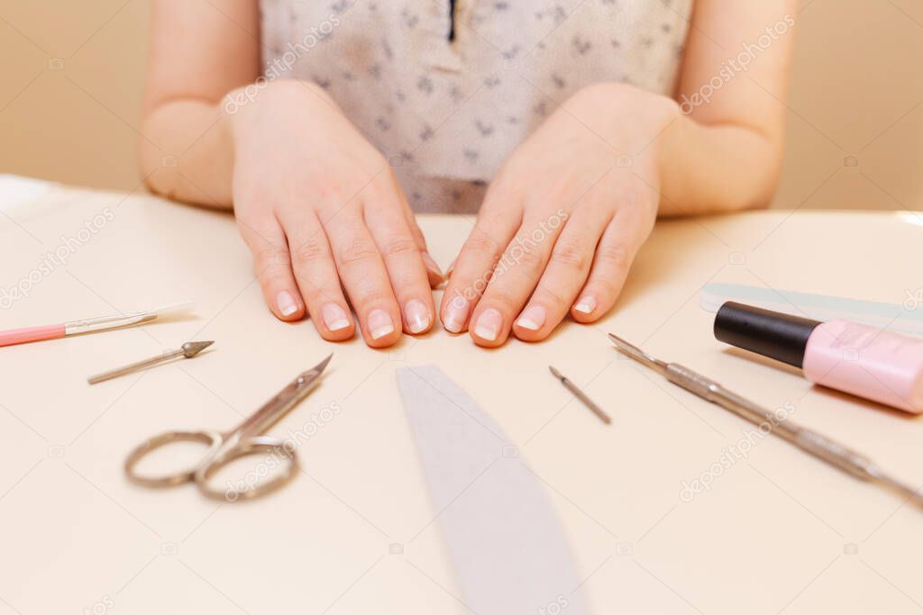 Medicine, cosmetology and manicure. A client in a nail salon demonstrates well-groomed nails after the procedure. White table with tools. Close up.