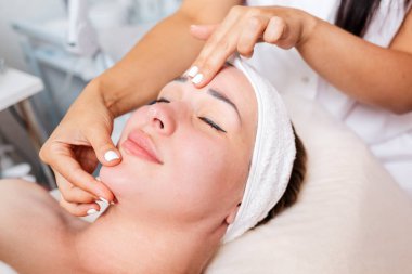 Güzellik salonu. Kozmetik uzmanı gülümseyen müşteriye yüz masajı yapar. Üst Manzara. Yüzünüzü kapatın. Profesyonel kozmetoloji kavramı.