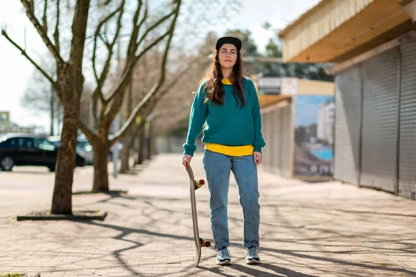 若い白人のヒップスター女性がスケートボードにもたれて立っている 背景には路地がある スポーツライフスタイルとストリートカルチャーの概念 — ストック写真