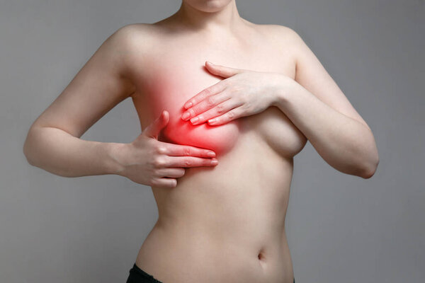 A young woman conducts an independent examination of the breast due to pain. Gray background. The concept of women's breast diseases.