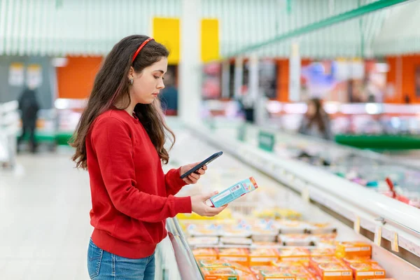 A young Caucasian woman scans the qr code on the package with a semi-finished product. Concept of modern technologies and shopping.