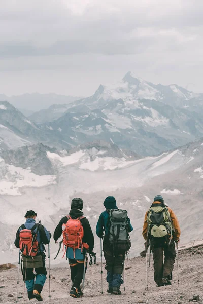 Extreme recreation and mountain tourism. A group of four tourists walking on a mountain trail. In the background, large snow-capped mountains. The view from the back.