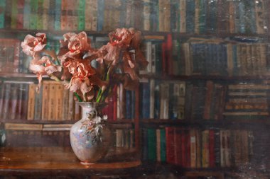 Kitaplığın arka planındaki vazoda süsen çiçekleri. Eski.