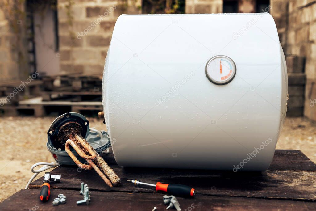 boiler disassembled, lying next to the heating element, nuts and tools on wooden surface ,outside.