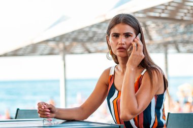 İletişim. Korkmuş bakışlı şık bir kadının portresi sahildeki bir yazlık kafede oturup telefonla konuşuyor. Sahtekarlık çağrıları kavramı.