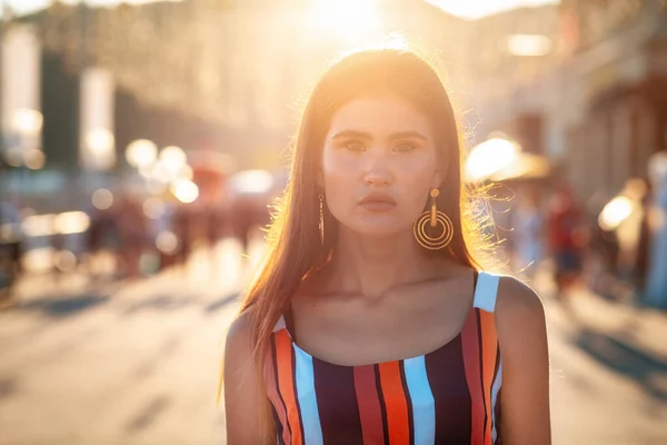 Portrait of a tanned woman in dress walking down the street.In the background, the sunset light and people in a blur. Concept of social advertising, travel and vacation.