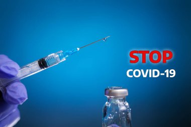 COVID-19 'u durdurun. Doktorun elinde iğne için bir şırınga var. Yanında da ilaç şişesi. Mavi arka plan. Koronavirüs, aşı ve sağlık konsepti.
