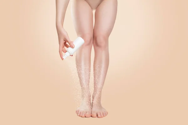 omen\'s smooth legs, and a hand that sprays cosmetics or medicine on the foot. Beige background. Copy space. The concept of freshness, hydration and protection of the skin of the feet.