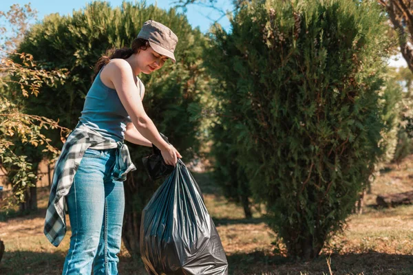 The concept of environmental pollution and Earth day. A female volunteer cleans the Park, collecting garbage bags in one place. Close up.