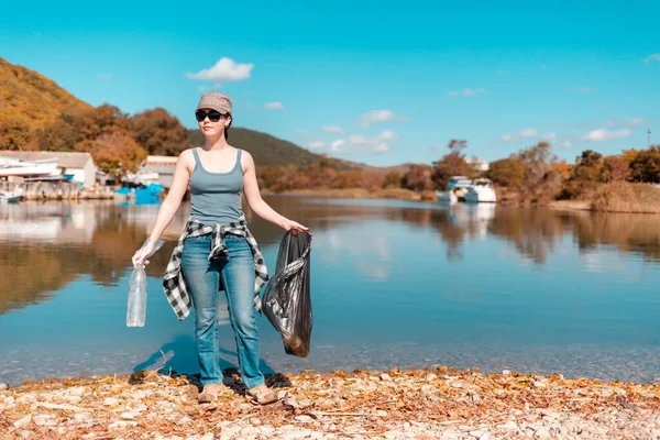 Ecology and garbage collection. Woman volunteer with a garbage bag in his hands, engaged in garbage collection on the lake or sea.