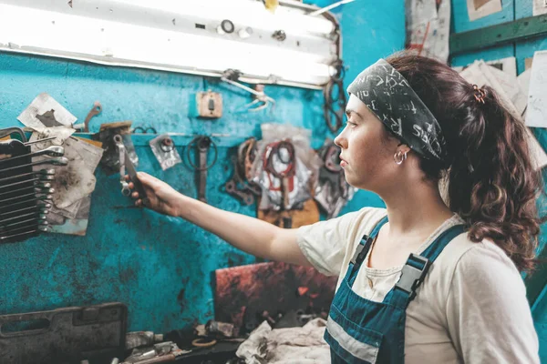Gender equality. Portrait of a young smiling woman in uniform working in a workshop, who takes tools from a tool box on the wall.