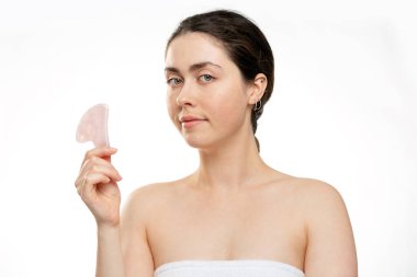 Gua Sha Masajı. Genç bir kadın elinde bir kuvars taşı guasha tutuyor, yarım dönüşlü bir portre. Beyaz arka plan. Geleneksel tıp ve kozmetoloji kavramı.