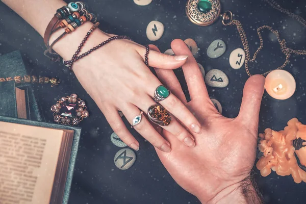 Astroloji ve ezoterizm. Falcı bir adamın avuç içini okur. Siyah arka planda runikler, bir mum, tılsım ve bir kitap var. Yukarıdan manzara. Kapatın. Havadaki toz..