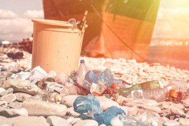 Kumsalda çöp bidonları ve dağınık plastik şişeler. Arka planda bir gemi var. Kapat..