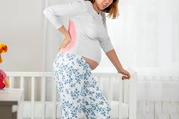 妊娠中の女性は背中の小さな手を握っており 赤ん坊のクレードルにもたれている 下の背部は赤いゾーンでマークされています 閉めろ 妊娠中の女性 母親の健康の概念 — ストック写真