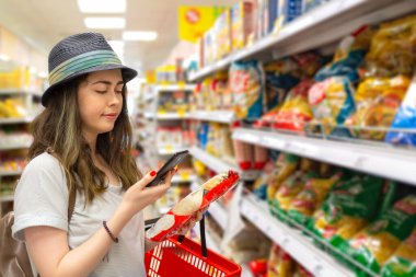 Genç ve güzel bir kadın süpermarketten ürünler seçiyor ve etiketteki QR kodunu kontrol ediyor. Mağazadaki modern teknoloji ve alışveriş kavramı.